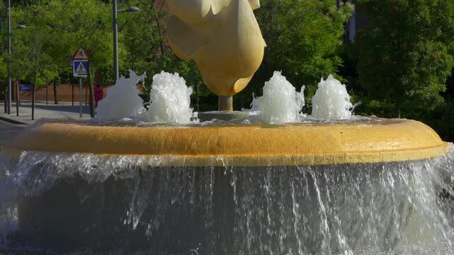 Slow motion water cascading from a yellow sculptural fountain on a sunny city street