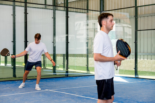 Male players compete in a doubles padel match indoors