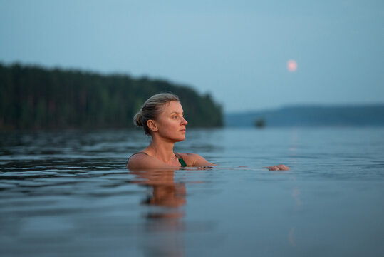 Woman swim in calm river during blue evening twilight