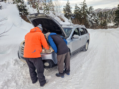 Ski travelers inspect car engine on snowy mountain road