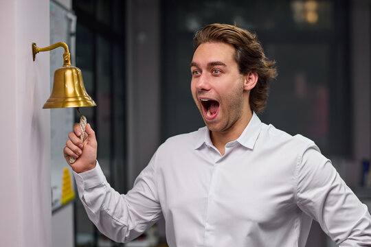Young man ringing brass service bell with excited expression inside office or restaurant interior, with man, adult, male, shirt detail, showing dress, trouser, black, white context