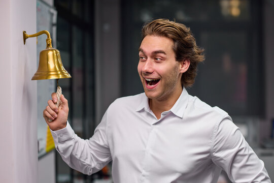 Young man ringing brass service bell with excited expression inside office or restaurant interior, with man, adult, male, shirt detail, showing dress, trouser, black, white context