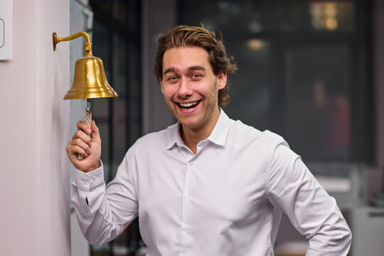 Young man ringing brass service bell with excited expression inside office or restaurant interior, with man, adult, male, shirt detail, showing dress, trouser, black, white context