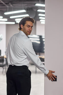 Young professional man swiping access card to enter modern office corridor during workday with focused expression and secure interior access, with man, professional, young, swiping detail