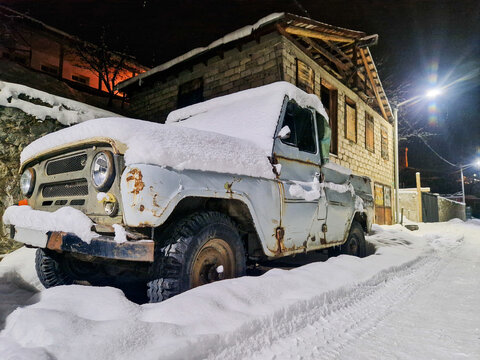 Snow-covered vintage truck beside a rustic house at night