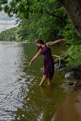 Fototapeta premium Woman Dancing at Lake Shore in Purple Dress Among Trees and Summer Nature