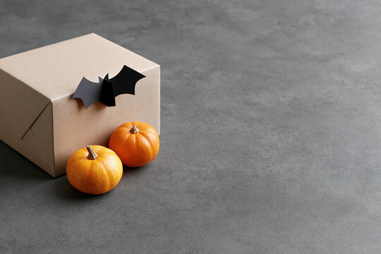 Halloween delivery concept with cardboard package, orange pumpkins and black paper bat decoration on gray background with copy space