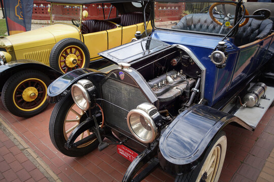 Blue 1914 Maxwell Model 25 vintage open touring car oldtimer with open hood section parked next to yellow 1910s Unic automobile, front three quarter view, Palic, Serbia, Jul 5, 2026