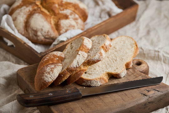 Rustic artisan bread slices with knife on wooden board