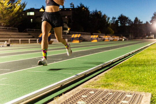 Woman run on illuminated athletics track at dusk