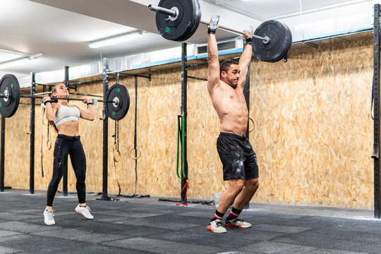 Athletic couple perform barbell lifts during gym workout