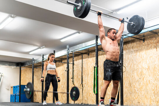 Athletic couple training with barbell in modern gym