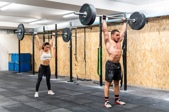 Couple perform barbell overhead lift during gym workout