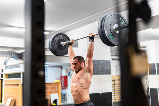 Male athlete lift barbell overhead in gym training