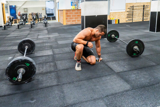 Exhausted athlete kneel beside barbell after workout