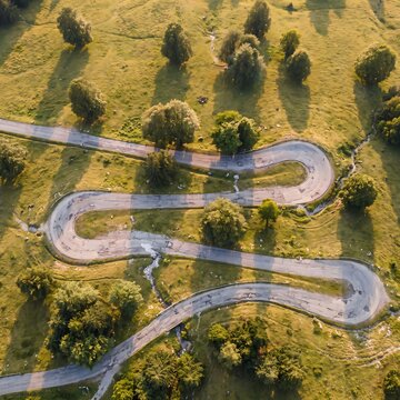 Aerial top down view of a sharp hairpin switchback road winding through a grassy rural mountain landscape with switchback