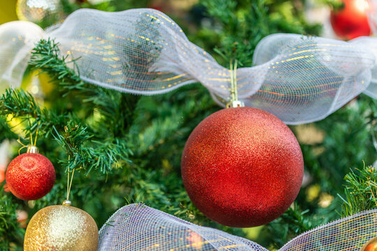 Sparkling red Christmas ornament hanging on a decorated pine tree with white ribbon