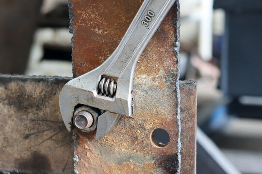 Adjustable wrench tightening a metal nut on a rusty plate.