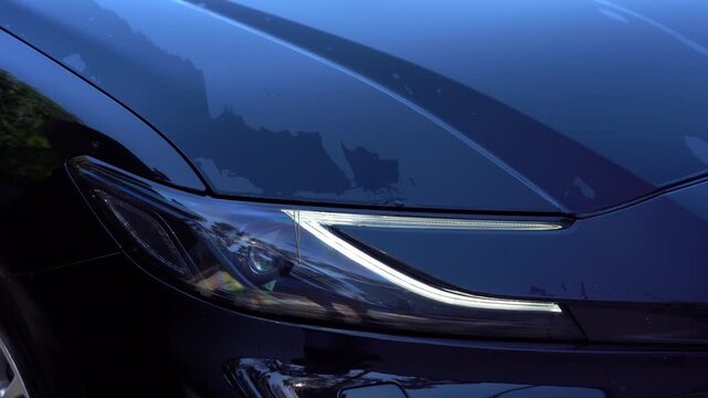 Close up of a person cleaning and polishing the headlight of a black car with a cloth