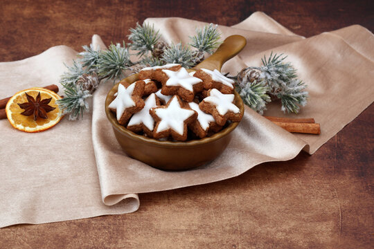  Eine Schale mit traditionellen Zimtsternen auf einem beigen Satintuch mit weihnachtlichen Gew&uuml;rzen und Tannenzweigen.