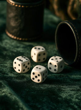 Vintage dice rolling game with white cubes and black leather cup on dark green velvet surface.