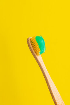 Bamboo toothbrush with green toothpaste on yellow background