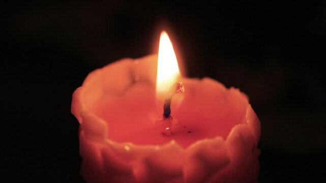 Serene scene with flickering candle and blurred background objects. Gentle lighting from candle creates inviting atmosphere with textured shadows and reflections