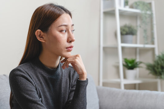 Unhappy anxiety young Asian woman covering her face with pillow on the cough in the living room at home.