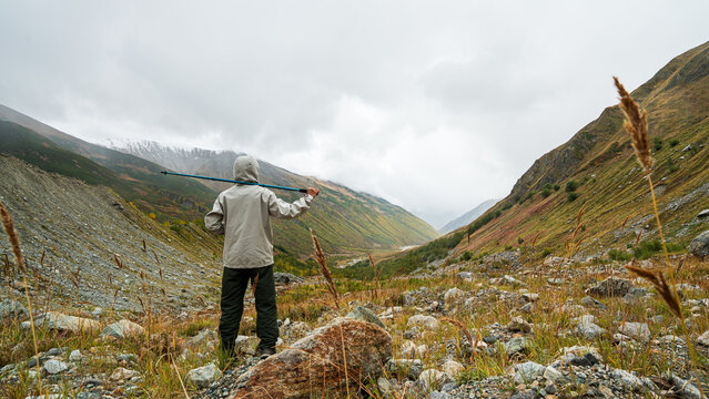 Hiker carrying a trekking pole through a rugged mountain valley near Shkhara Glacier in Svaneti, Georgia