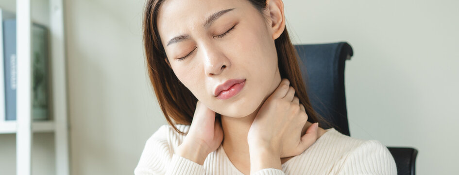 Asian business woman suffering from neck pain working in office sitting at table.