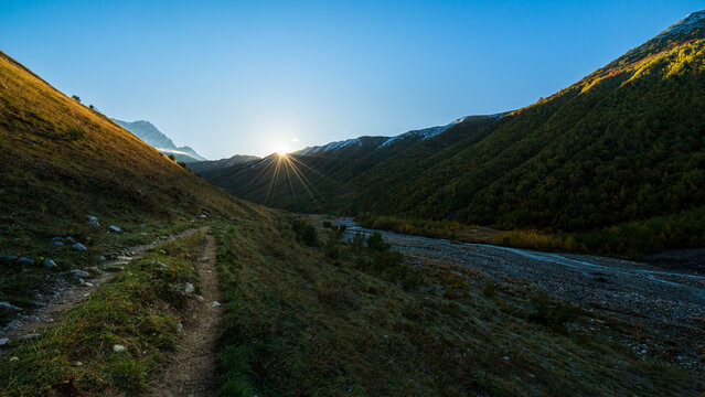Landscape photograph of sunrise with sunstar flare over mountain valley and hiking path near Adishi Glacier in Svaneti Georgia.