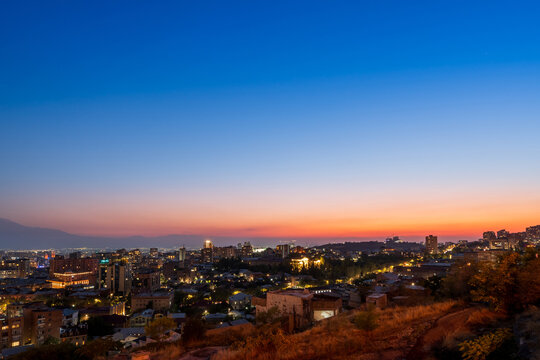 Twilight cityscape photograph of Yerevan skyline with vibrant orange and blue sky at dusk from Yerevan Cascade in Armenia.
