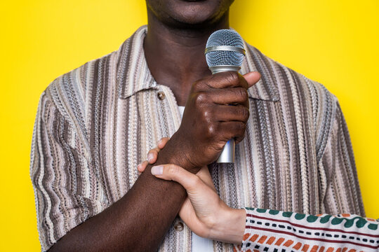 Multiethnic hands hold microphone against yellow background