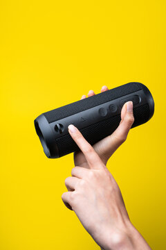 Woman hands adjust portable Bluetooth speaker on yellow background