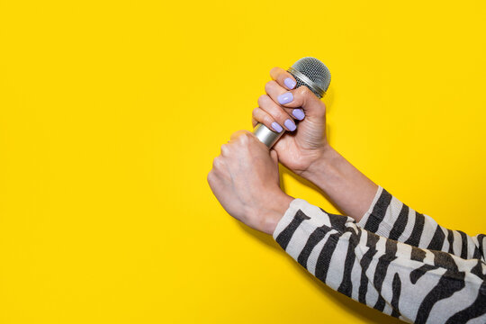 Woman hand holding microphone on yellow background