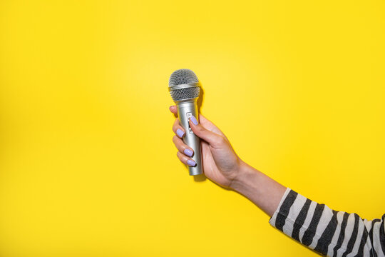 Woman hand hold microphone against bright yellow background