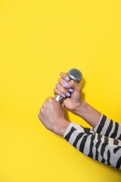 Woman hand holding microphone against yellow background