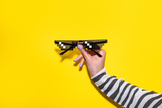 Woman hand hold pixel sunglasses on yellow background