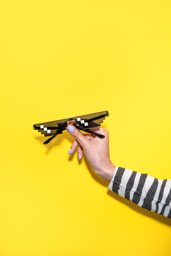 Woman hand hold pixel sunglasses on yellow background