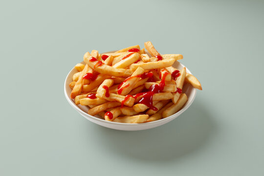 French fries with ketchup in white bowl on green background