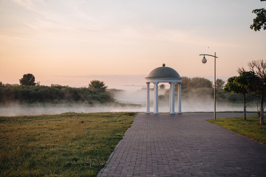 Sunrise over misty river with white pavilion in summer