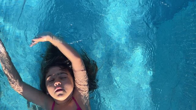 Horizontal top view video of a girl floating relaxed in a swimming pool
