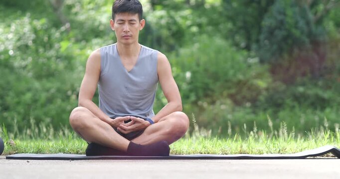 Peaceful athletic man meditating with dhyana mudra hands on mat in park