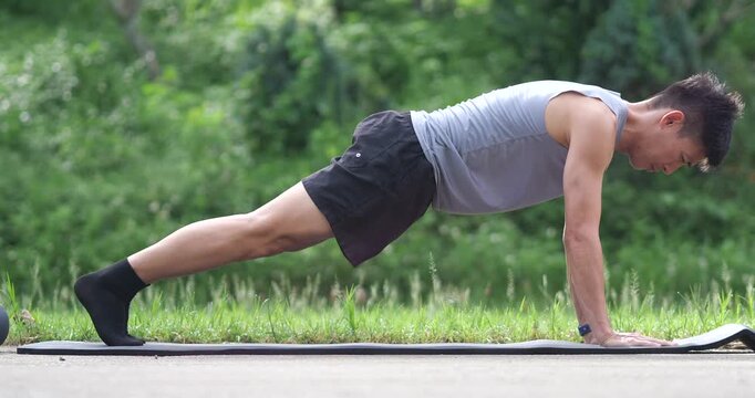Side view of athletic man holding high plank push up position on mat in park
