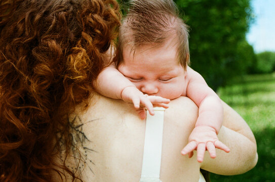 Baby on woman's shoulder in а green park