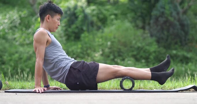 Side view of athletic man rolling calf muscle with foam roller in park