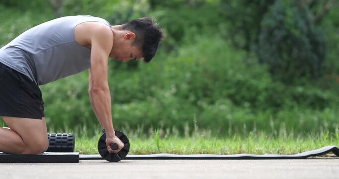 Side view of athletic man doing ab wheel rollout workout on grass in park