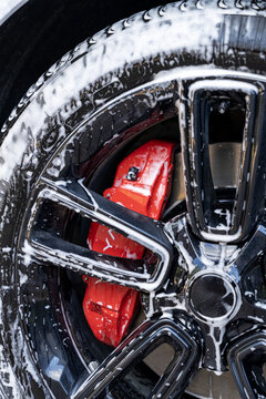 Close-up of soapy car wheel and red brake caliper