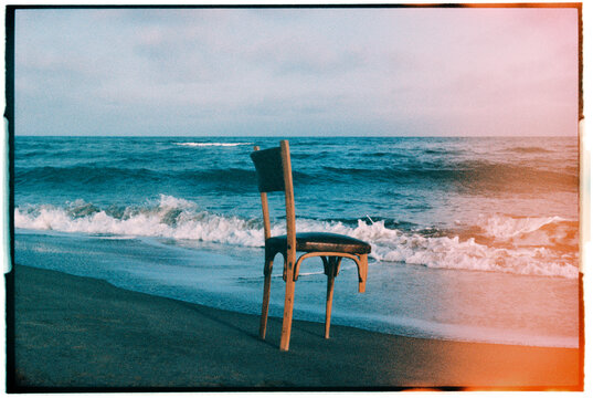 a damaged wooden chair beside breaking waves, 35mm film