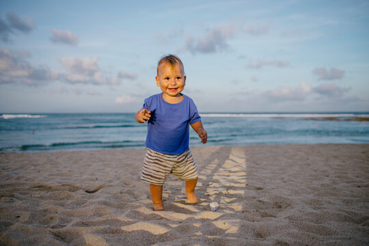Happy toddler boy taking his first steps on a sandy beach
